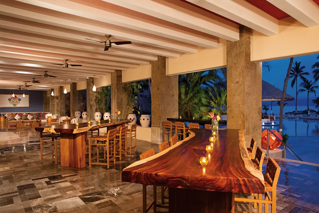 Veranda Terrace Bar at Sunscape Puerto Vallarta Resort & Spa featuring an open-air bar with wooden tables, garden views, and oceanfront scenery.